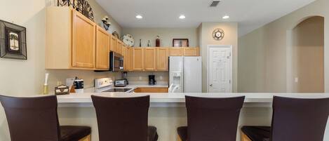 A kitchen with wooden cabinets, a white refrigerator, a coffee maker, and three bar stools.