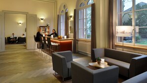 Un vestíbulo de hotel con área de bar, disposición de asientos y amplios ventanales con vistas al exterior.