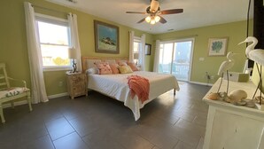 A bedroom with a bed, a nightstand, a chair, a ceiling fan, and a view of the outdoors.