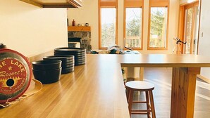 Una cocina con una mesa de madera y taburetes, una chimenea de piedra y un ventanal con vistas a árboles.