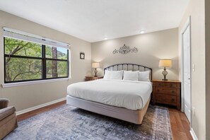 Une chambre avec un grand lit, deux tables de chevet avec des lampes, une fenêtre avec des stores et un tapis à motifs.