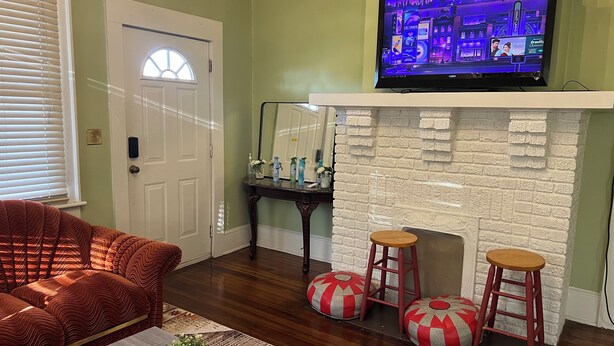 Ein Wohnzimmer mit Fernseher über einem Kamin, einer Tür und einem gemusterten Sofa.