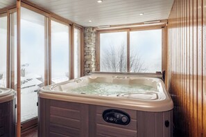 A hot tub in a room with wooden walls and large windows.