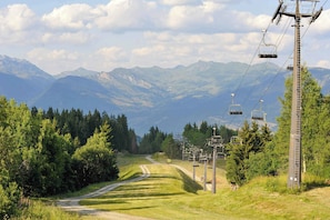 Strada di montagna con una seggiovia e paesaggio boscoso.