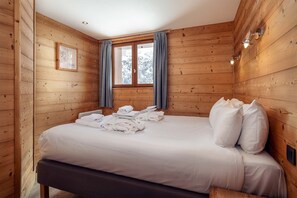 Quarto de cabana de madeira com cama, toalhas e janela com cortinas.