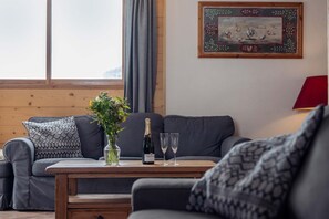 Uma sala de estar com uma mesa de madeira, um sofá, um vaso com flores e uma garrafa de champanhe.
