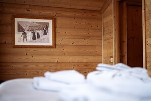 A wooden cabin interior with a framed photograph on the wall, a bed with white bedding, and a wooden door.