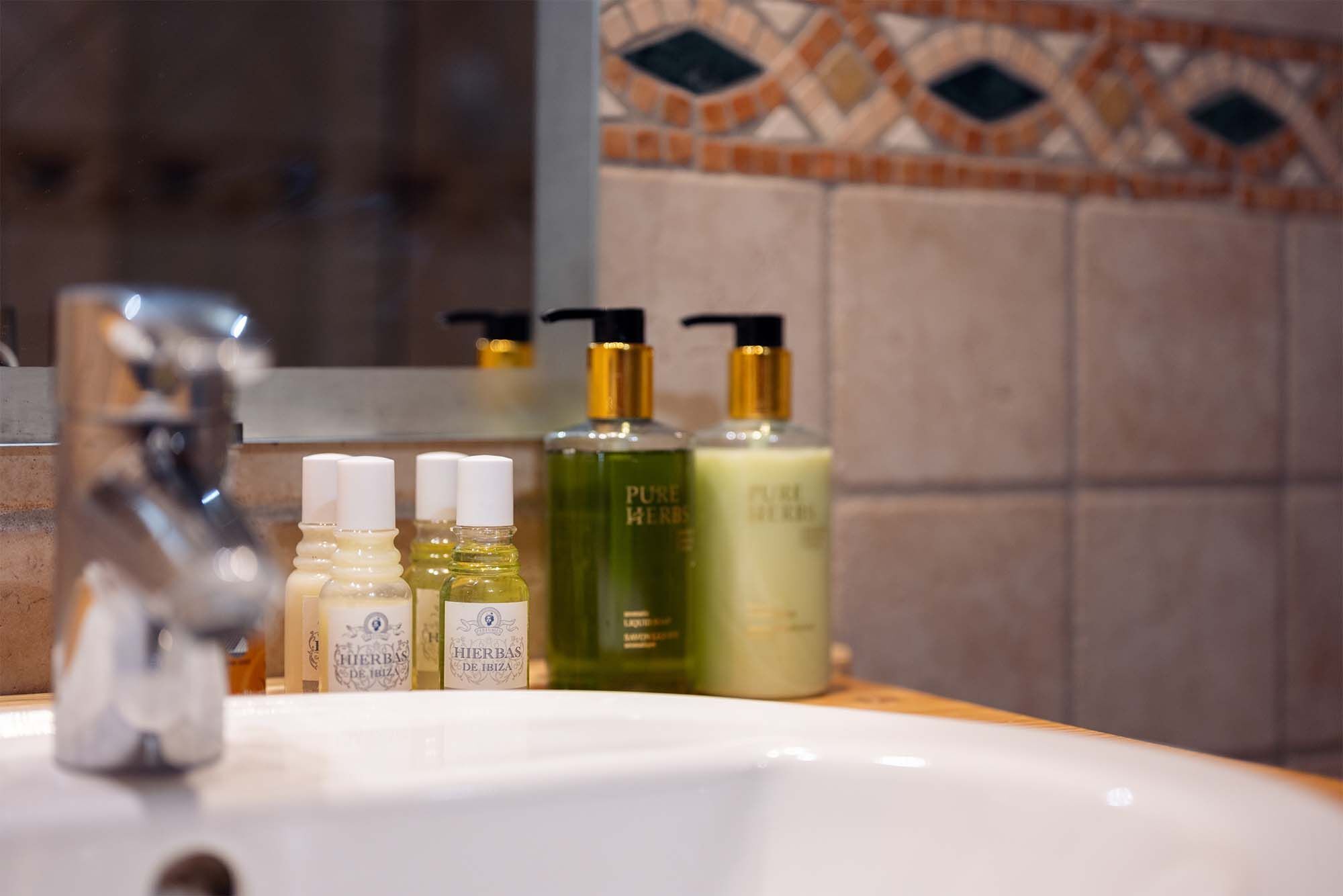 Un lavamanos de baño con varios artículos de aseo, incluyendo una botella etiquetada 'PURE HERBS' y un grifo.