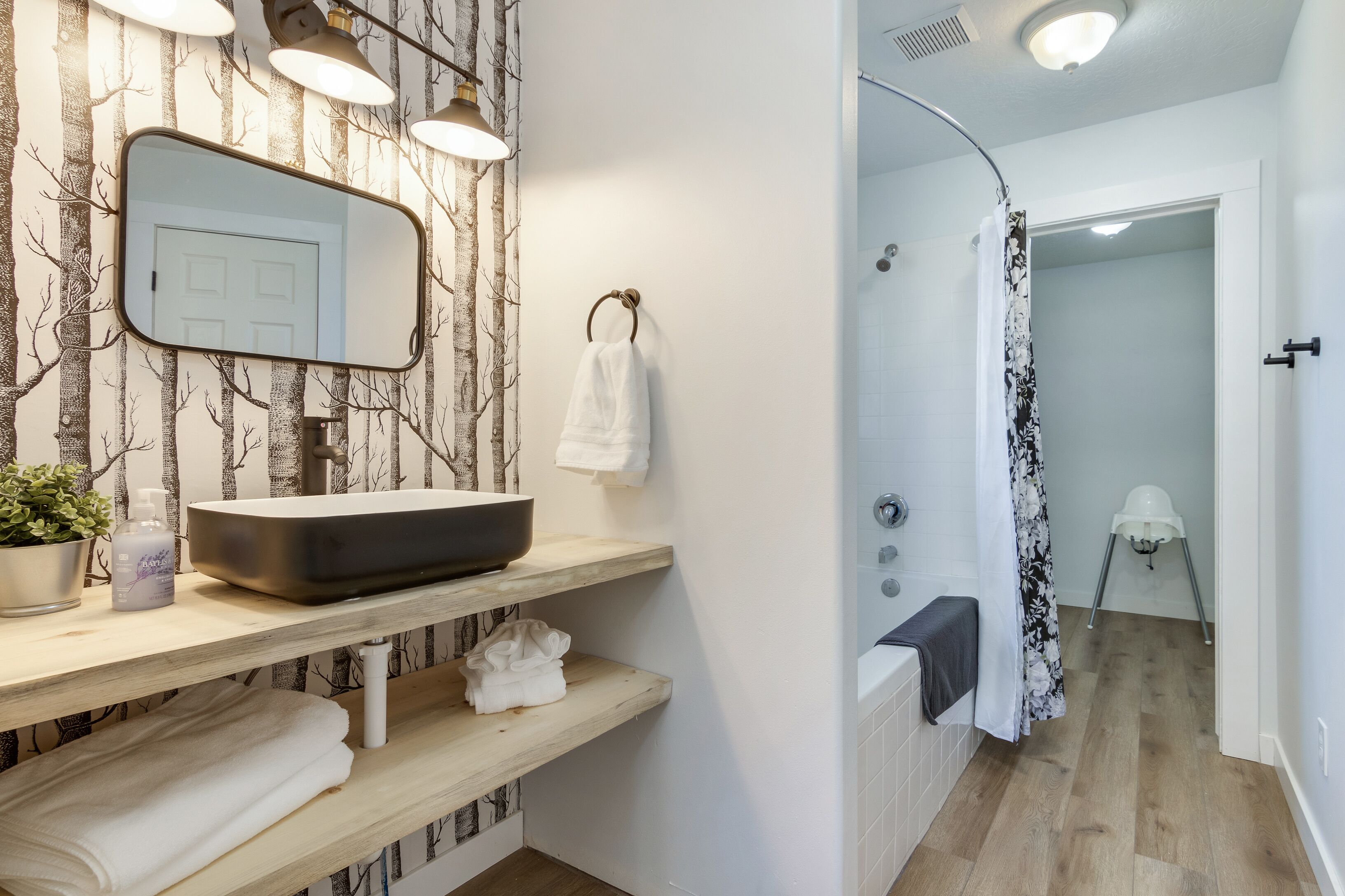 Een moderne badkamer met een grote spiegel, houten planken, een zwart wastafelmeubel en een douche met gordijn.