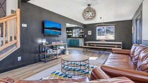 Een moderne woonkamer met een leren bank, een ronde salontafel en een aan de muur bevestigde televisie.