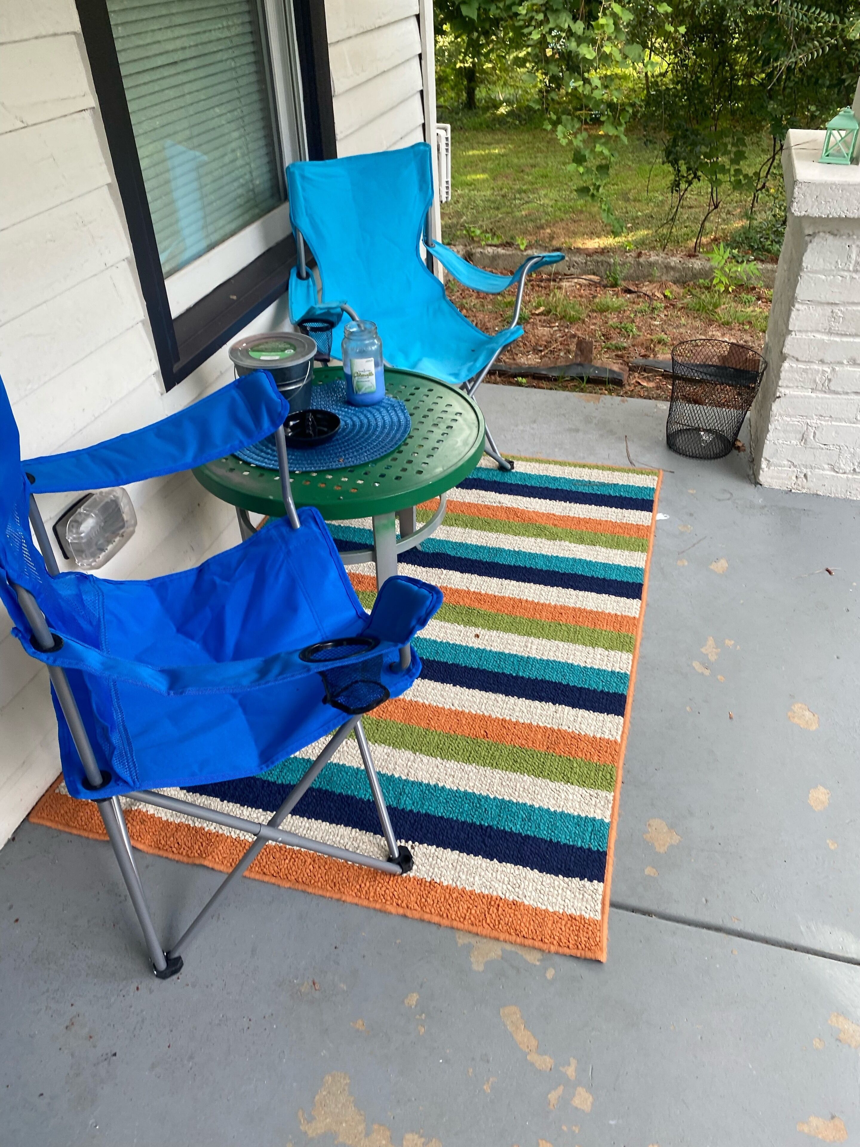 Een terras met twee blauwe stoelen, een groene tafel en een gestreept kleed.