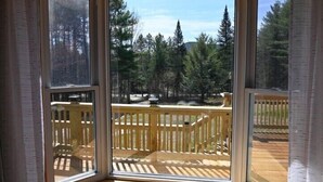Quarto nos fundos, com amplas janelas que oferecem vista para um deck de madeira e árvores ao redor.