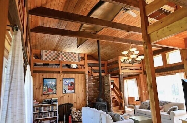 A rustic cabin interior with wooden beams, a fireplace, a staircase, and a cozy seating area. - Shepherds River Lodge (Brownfield)