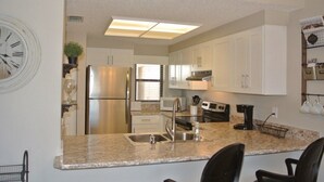 A modern kitchen with white cabinets, stainless steel appliances, a granite countertop, and a clock on the wall. - Ocean Village Club I33, Elevator, 2 Pools (1 Heated) Ocean View (St. Augustine)