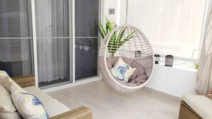 A modern living room with a hanging chair, a sofa, and a large window with sheer curtains. - Close to the Beach! (Punta Cana)