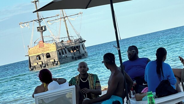 A group of people sitting under an umbrella by the sea, with a ship in the background. - Close to the Beach! (Punta Cana)