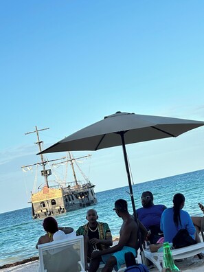 A group of people sitting under an umbrella by the sea, with a ship in the background. - Close to the Beach! (Punta Cana)