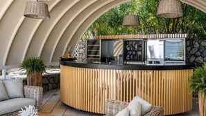 Zona de bar con forma curva, un fondo de piedra, mobiliario de mimbre y vistas a la vegetación.