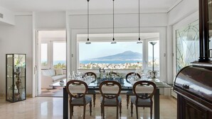Comedor con mesa lista para cuatro personas, ventanas amplias que ofrecen vistas a la ciudad y un piano en la esquina.