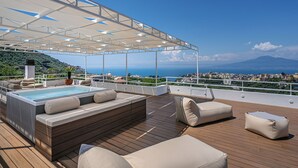 Una terraza en la azotea con jacuzzi, cubierta de madera y mobiliario exterior.