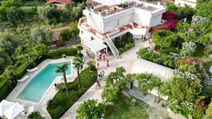 Un edificio moderno de varios pisos con terraza en la azotea, piscina y abundante vegetación alrededor.