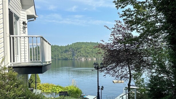 Ein Anwesen am Seeufer mit einem Balkon mit Blick auf das Wasser, einer Treppe, die zum Eingang führt, und Blick auf den umliegenden Wald.