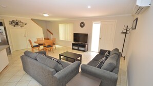 A living room with a sofa set, a coffee table, a TV, and a dining area with a table and chairs.