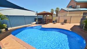 A backyard with a swimming pool, patio furniture, and a covered seating area.