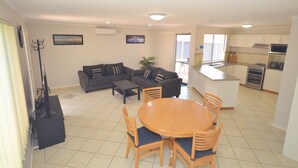 A modern living room with a sofa set, a dining table with chairs, a kitchen area with a microwave and stove, and a balcony with curtains.