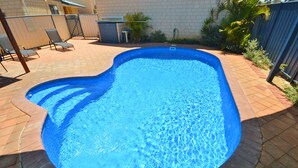 En swimmingpool med murstenskant, omgivet af en patio med stole og et lille bord.