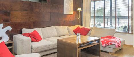 A modern living room with a sectional sofa, a coffee table, and a large window with blinds.