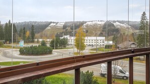 Vista desde una ventana con una calle y una rotonda, un edificio con un cartel de 'Sale' y una colina nevada al fondo.