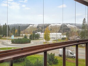 Une vue depuis une fenêtre donnant sur une route, avec un bâtiment portant l’inscription « Vente » visible au loin, entouré d’arbres et d’un paysage vallonné.