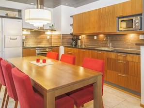 A modern kitchen with wooden cabinets, a stainless steel microwave, and a dining area with a wooden table and red chairs. - Tahko spa suites orange a 8 by Interhome (Nilsiä)
