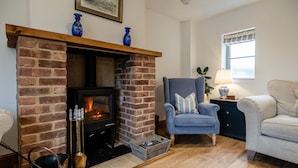 Un salón acogedor con chimenea de ladrillo, un sillón azul y suelo de madera.