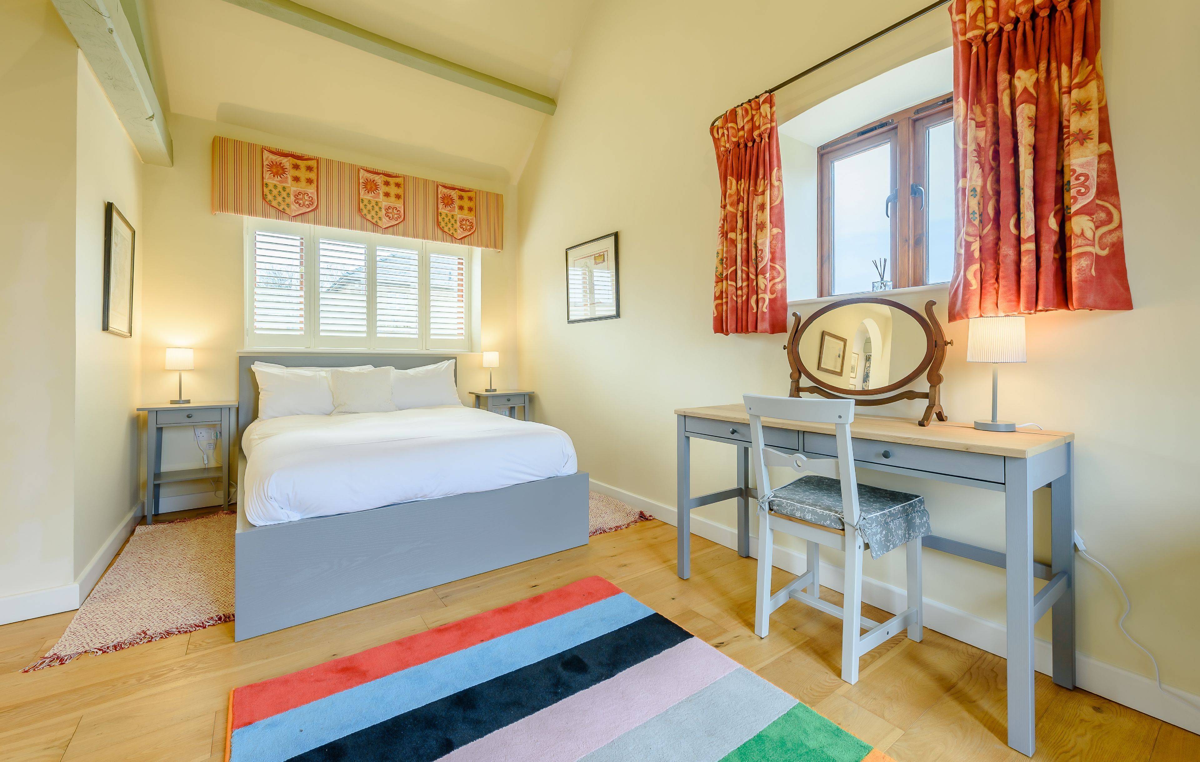 A bedroom with a bed, a desk, a chair, a window with curtains, and a lamp.