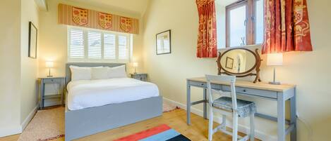 A bedroom with a bed, a desk, a chair, a window with curtains, and a lamp.