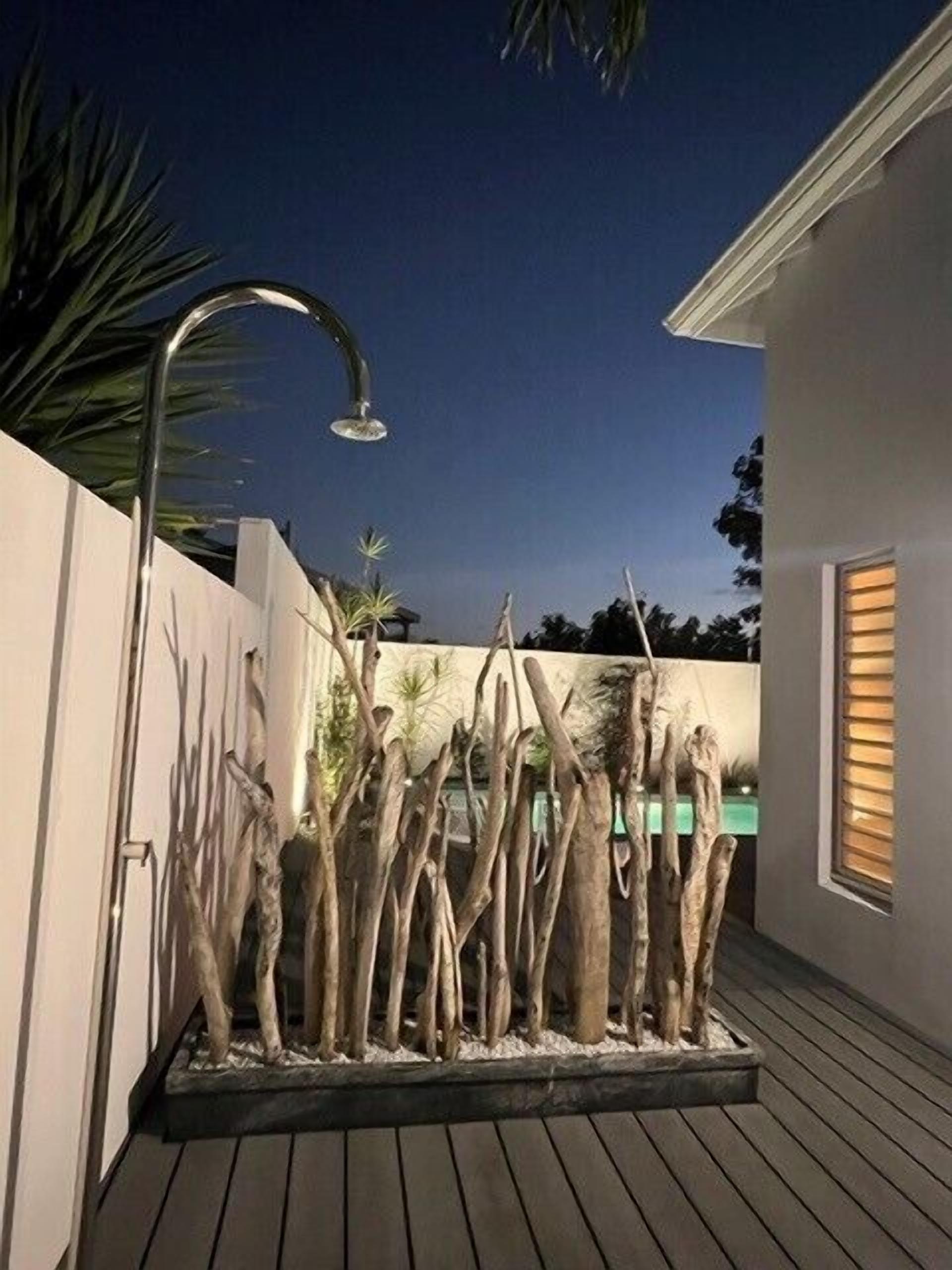 A modern outdoor area with a wooden deck, a decorative tree sculpture, and a metal showerhead.