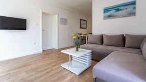Ein modernes Wohnzimmer mit einem Flachbildfernseher, einer Couch, einem Couchtisch mit Blumenvase und einem Meeresbild an der Wand.