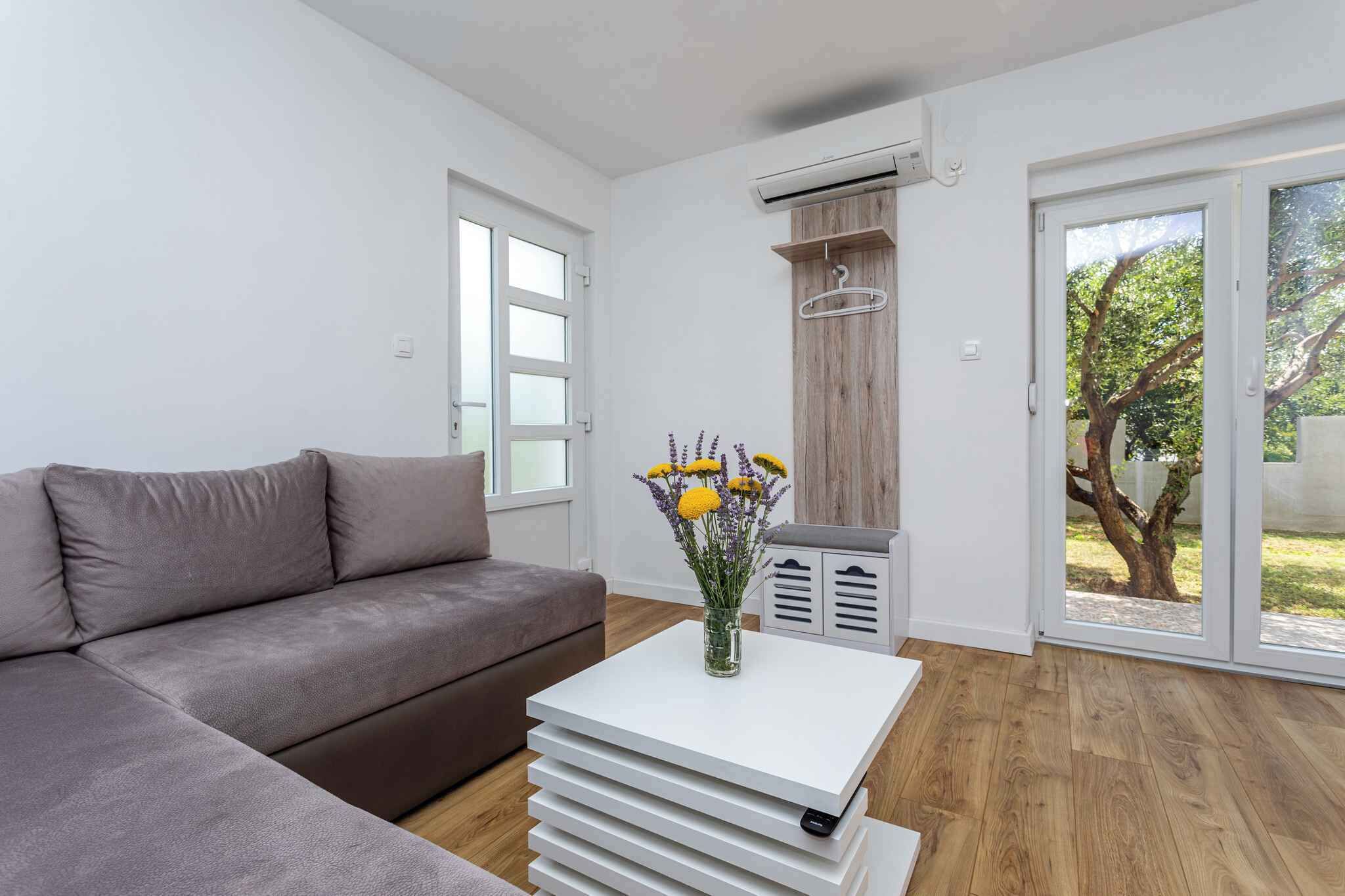 Ein modernes Wohnzimmer mit einem grauen Sofa, einem weißen Couchtisch mit Blumenvase und einer Schiebetür zu einem Garten.