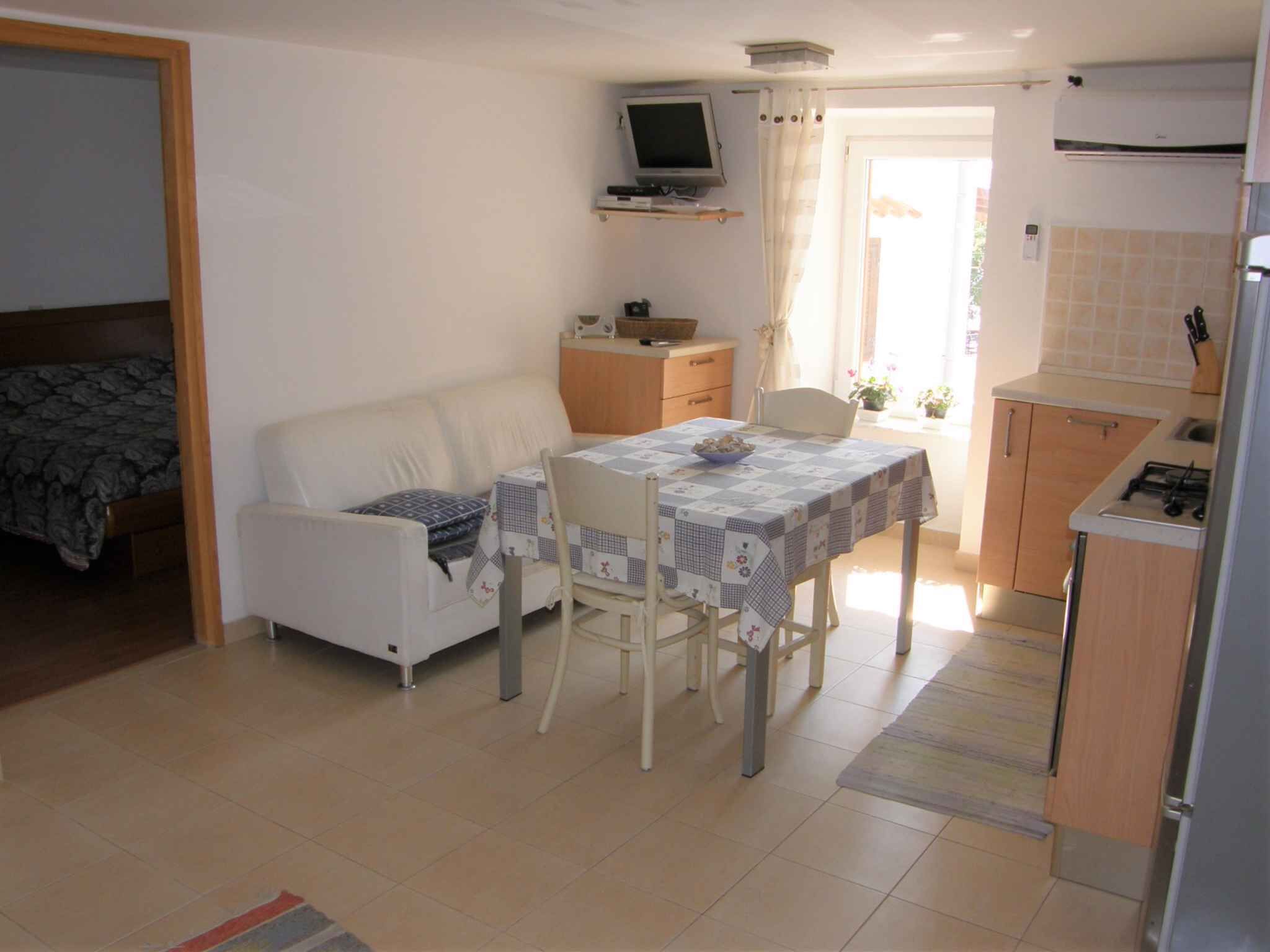 A compact living space with a dining area, kitchenette, and a television mounted on the wall.