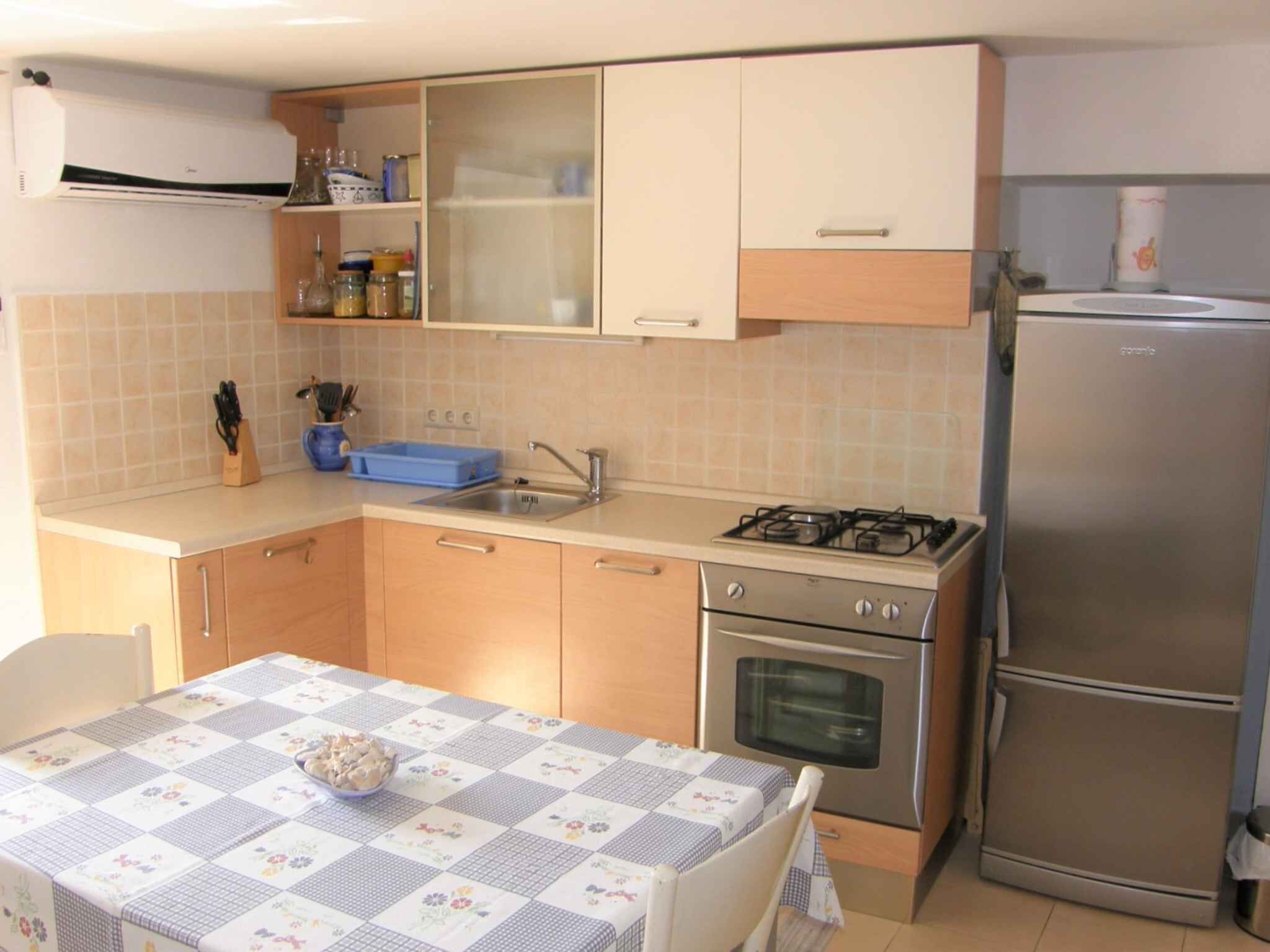 A compact kitchen with a gas stove, oven, and a built-in refrigerator. There is a sink with a blue soap dish and a table with a floral tablecloth.