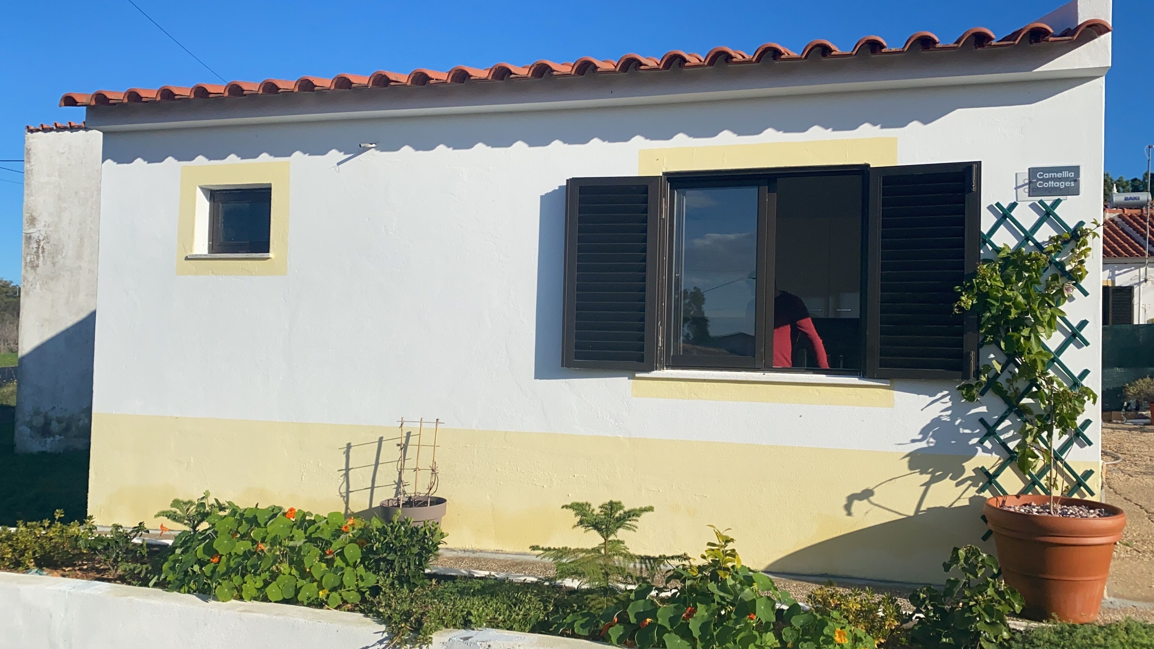 A building with a tiled roof, a small window, and a door. There is a sign that reads "Camellia Cottages."