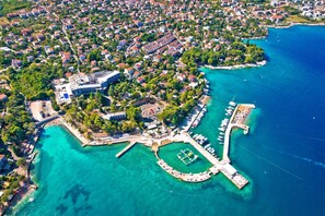 Eine Vogelperspektive einer Küstenstadt mit einem Yachthafen, Wohnhäusern und einem großen Hotel mit Innenhof.
