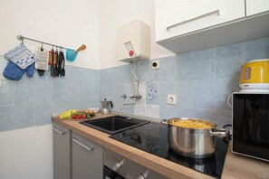 Eine Küche mit Spüle, Herd und Mikrowelle. Es befinden sich Küchenutensilien an der Wand und ein Topf auf der Arbeitsfläche.
