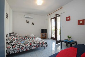 Camera d'albergo con un letto, una televisione, un tavolino con una pianta e una porta scorrevole verso l'esterno.