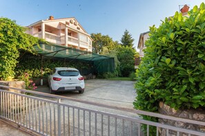 A white car parked in a driveway with a covered patio area and a building with a balcony in the background.
