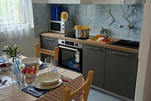 Et køkken med mikrobølgeovn, komfur og vask. Der er et spisebord dækket med tallerkener, glas og en vase med blomster.