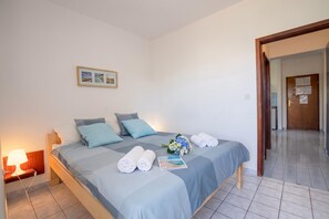 A hotel room with a bed, a nightstand, a lamp, a framed picture on the wall, and a door leading to another room.
