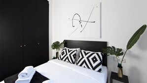 Un dormitorio moderno con un armario negro, una cama con almohadas estampadas, una obra de arte en la pared y una planta en maceta.